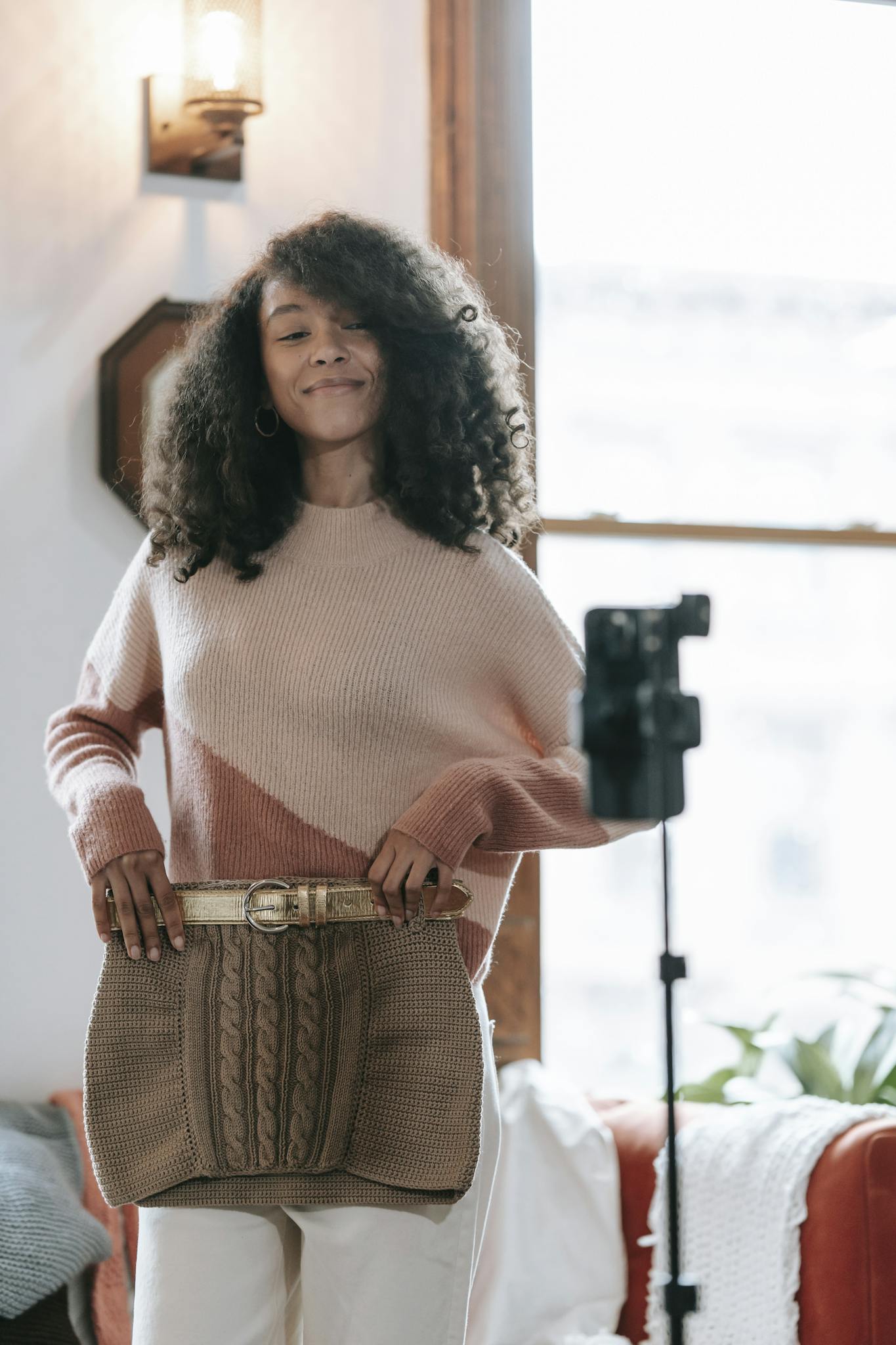 Cheerful young African American female vlogger with knitted skirt recording video on cellphone at home