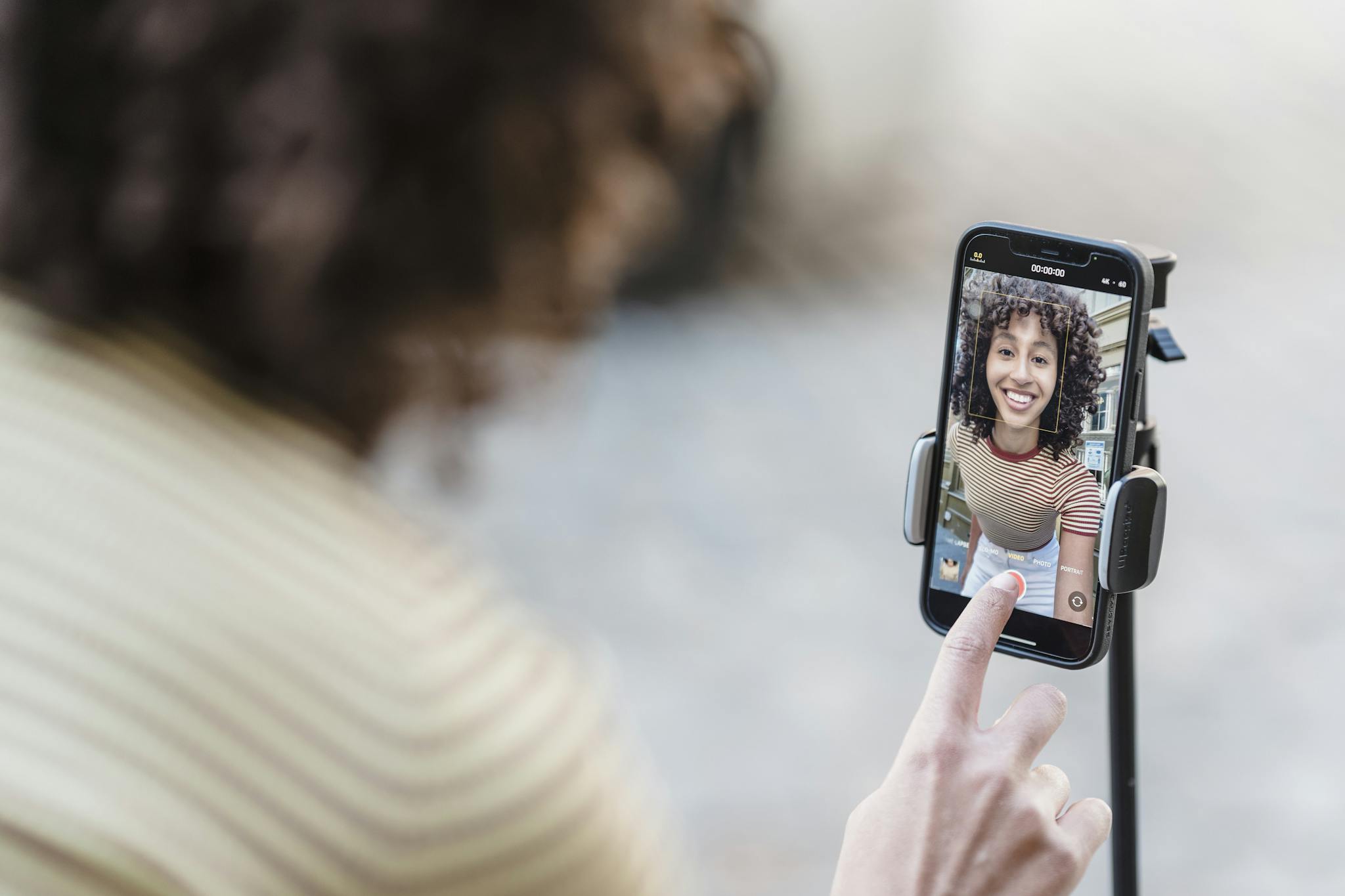 Crop cheerful young ethnic female vlogger touching screen on cellphone while preparing for video record in town